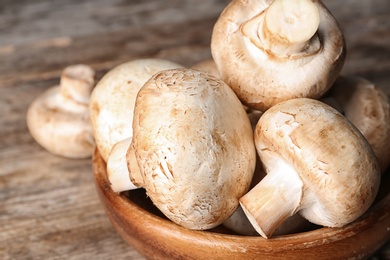 Bowl of fresh champignon mushrooms on wooden background, closeup