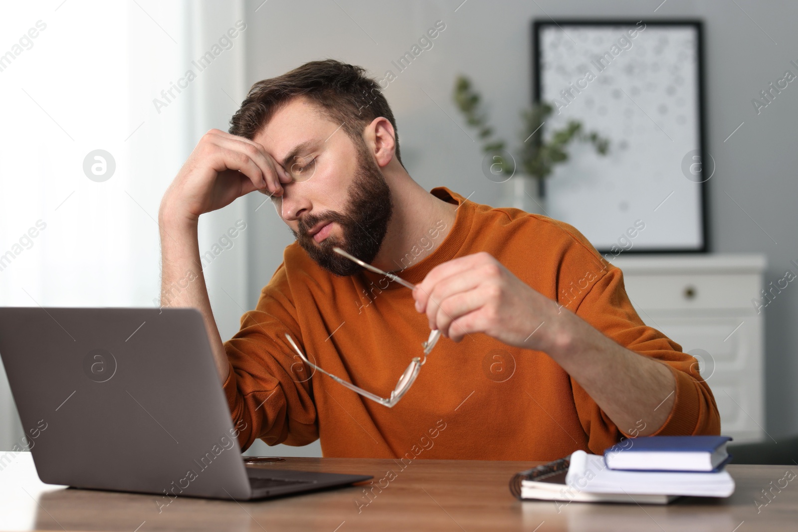 Photo of Overwhelmed man sitting with laptop at table indoors