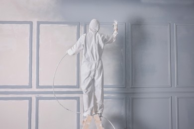 Photo of Decorator dyeing wall in grey color with spray paint, back view