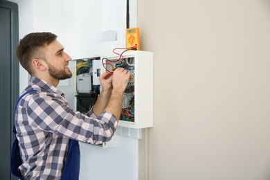 Photo of Electrician with tester checking voltage indoors, space for text