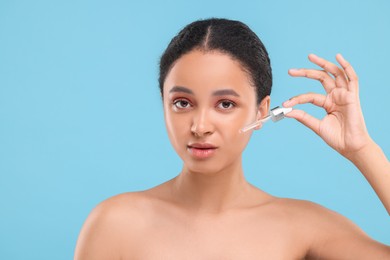 Beautiful woman applying serum onto her face on light blue background