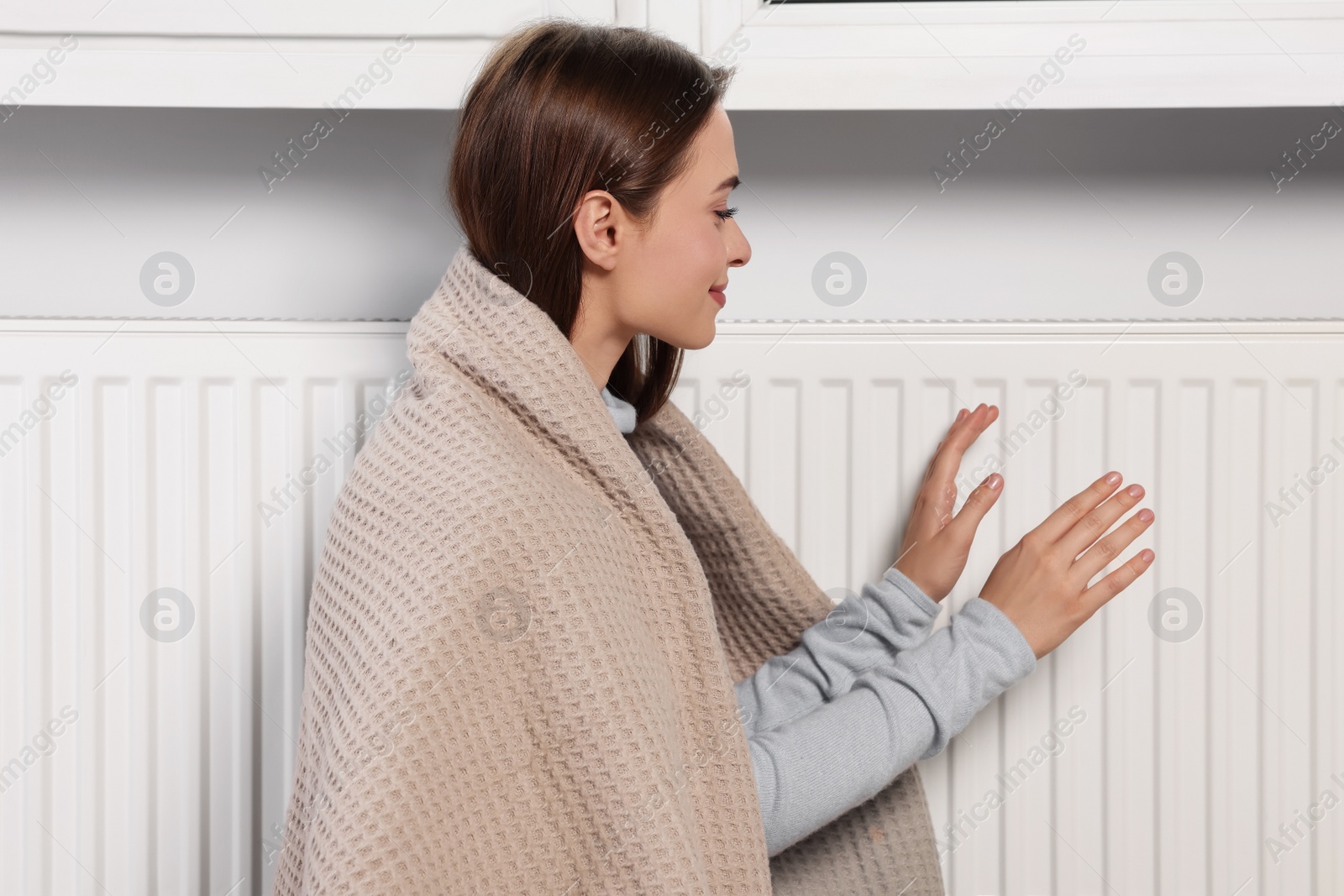 Photo of Woman warming hands on white heating radiator indoors