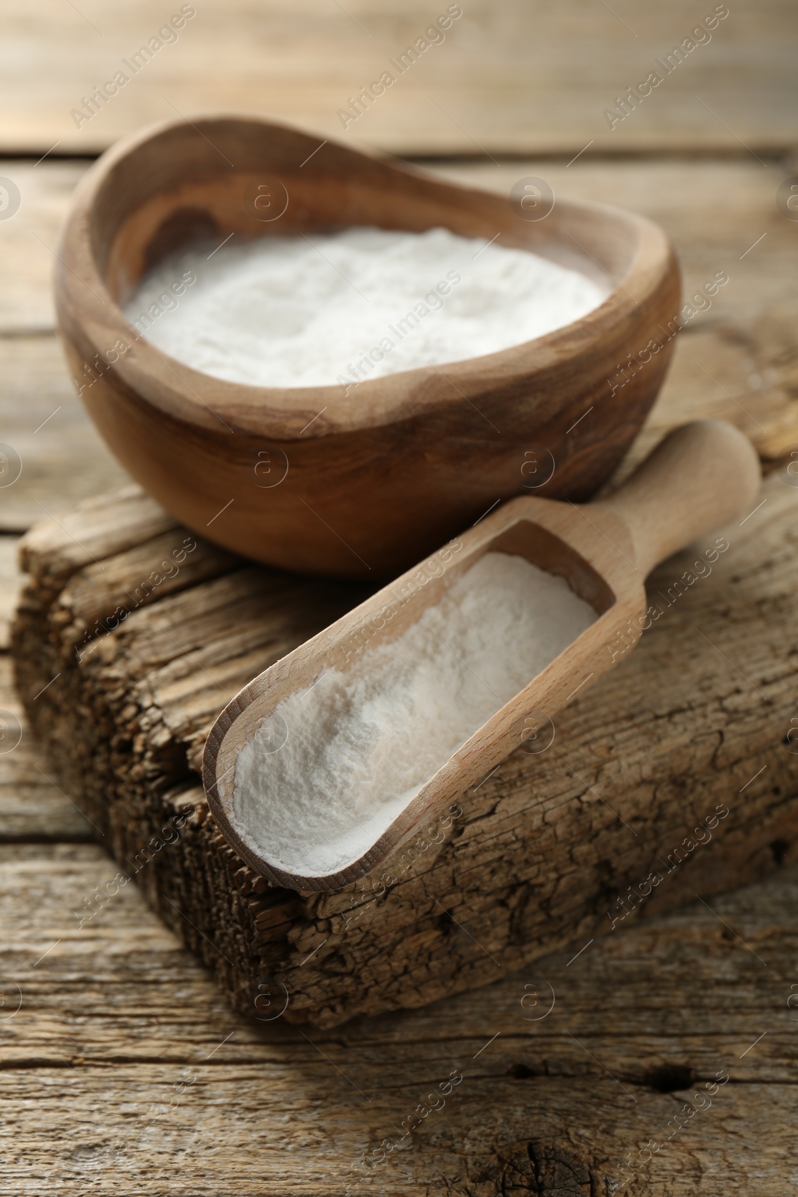 Photo of Baking powder in bowl and scoop on wooden table, closeup