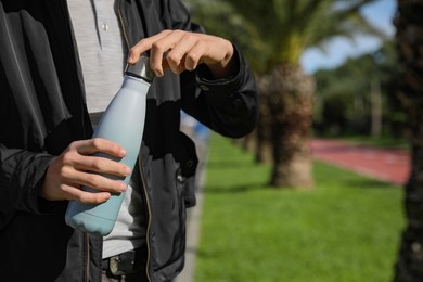 Photo of Man holding thermo bottle in park on sunny day, closeup. Space for text