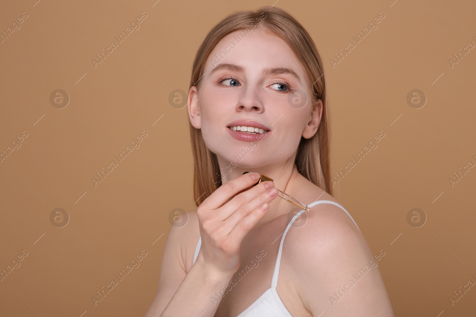 Photo of Beautiful young woman applying essential oil onto shoulder on brown background