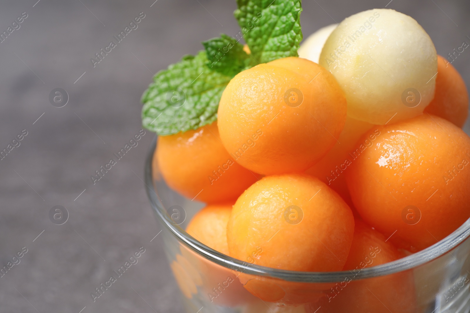 Photo of Melon balls and mint in glass on grey table, closeup. Space for text