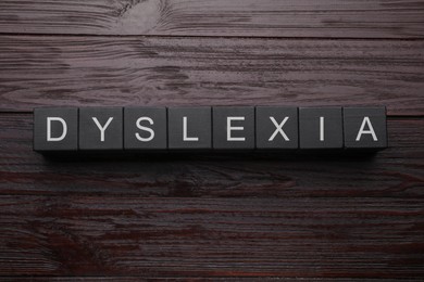 Photo of Black cubes with word Dyslexia on wooden background, flat lay