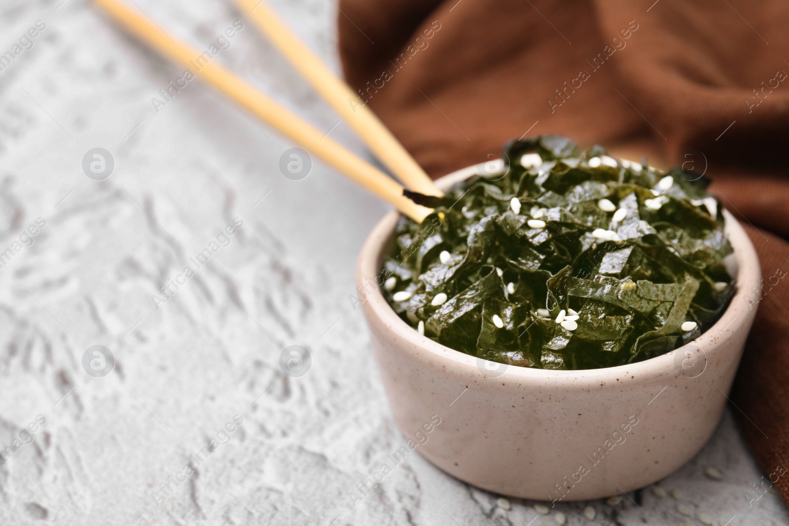 Photo of Chopped nori sheets with sesame and chopsticks on white textured table, closeup. Space for text