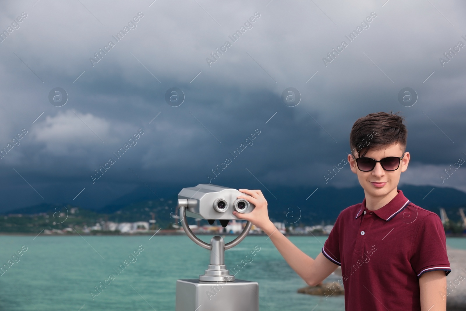 Photo of Teenage boy near mounted binoculars at sea. Space for text