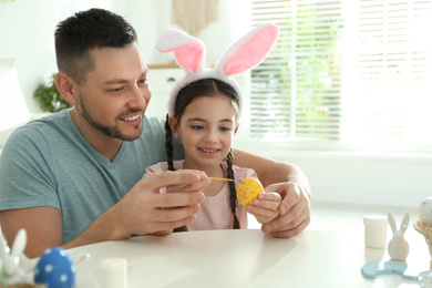 Photo of Happy daughter with bunny ears headband and her father painting Easter egg at home