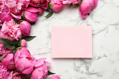 Fragrant peonies and blank card on marble table, top view with space for text. Beautiful spring flowers