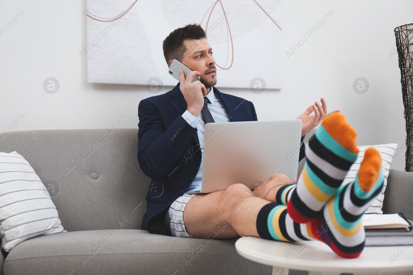 Photo of Businessman in shirt, underwear and funny socks talking on phone during video call at home