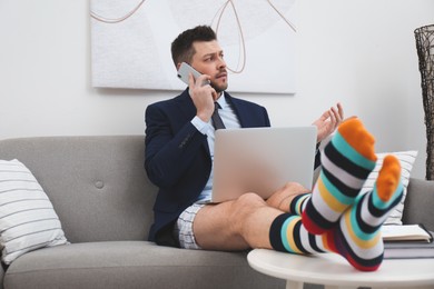 Businessman in shirt, underwear and funny socks talking on phone during video call at home