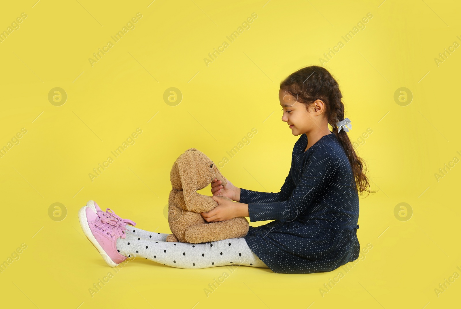 Photo of Cute little girl with toy bunny on yellow background