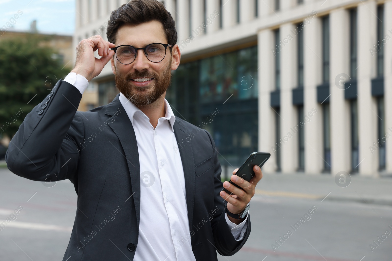 Photo of Handsome businessman with smartphone on city street, space for text