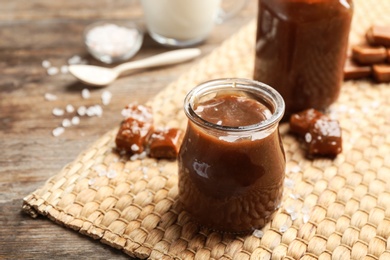 Photo of Jar of caramel sauce on wooden table. Space for text