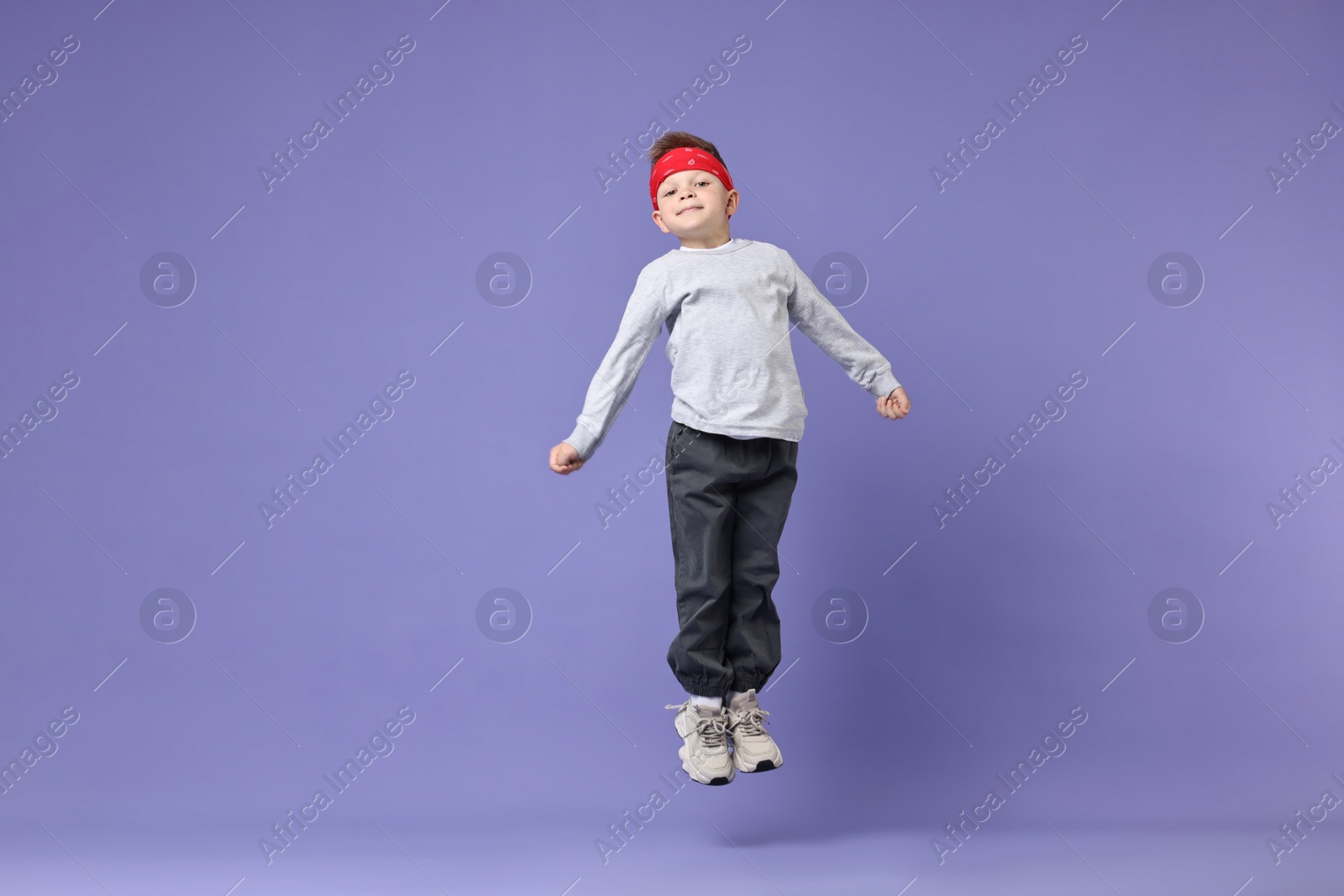 Photo of Happy little boy dancing on violet background. Space for text