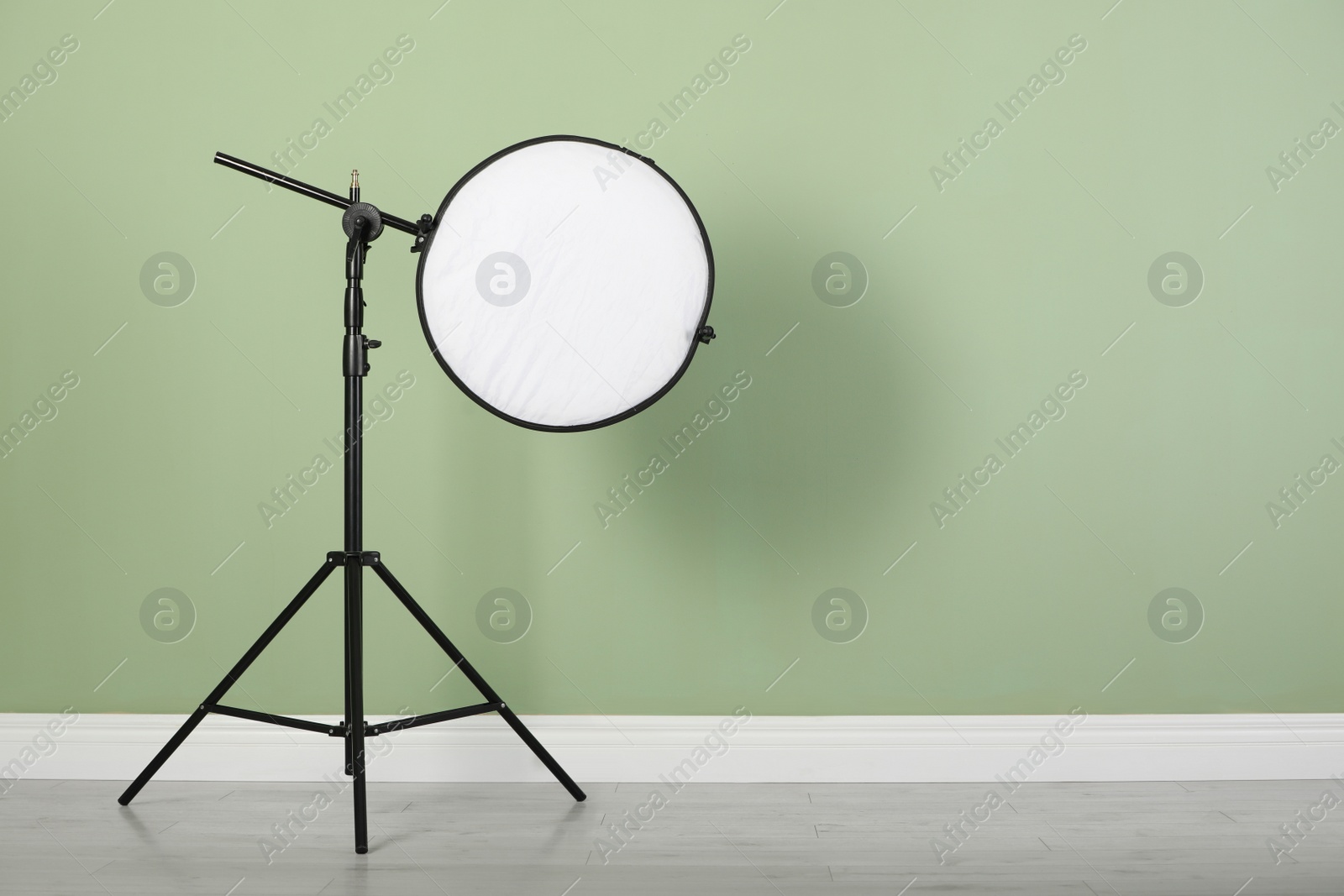 Photo of Studio reflector on tripod near pale green wall indoors, space for text. Professional photographer's equipment