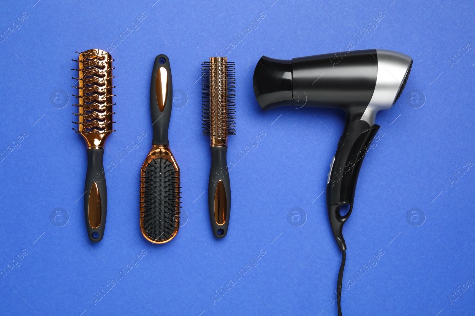 Photo of Hair dryer and different brushes on blue background, flat lay. Professional hairdresser tool