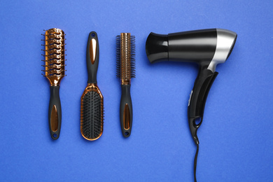 Photo of Hair dryer and different brushes on blue background, flat lay. Professional hairdresser tool