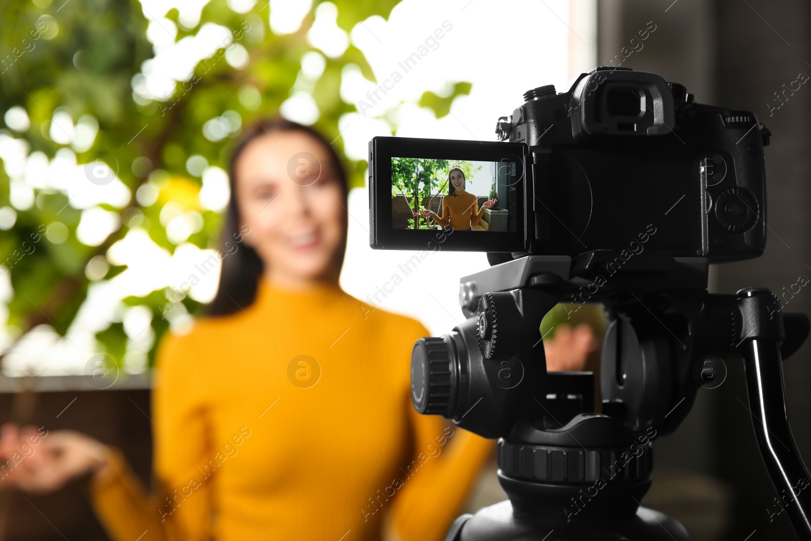 Photo of Young blogger recording video indoors, focus on camera screen