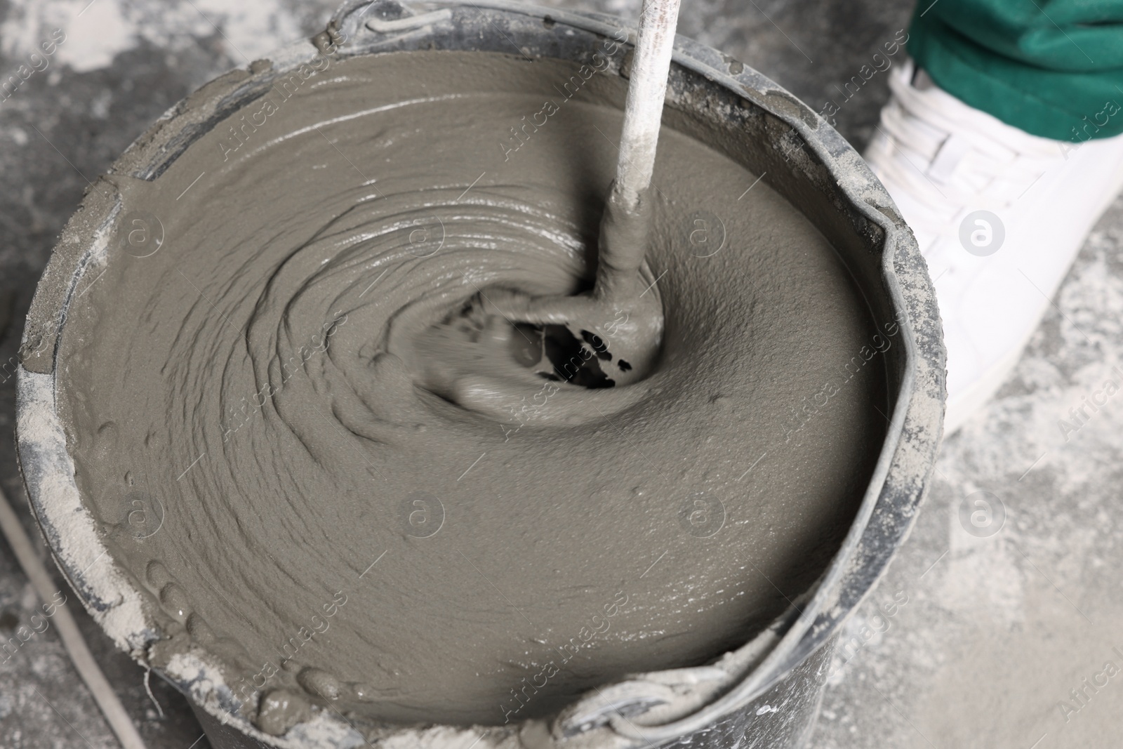 Photo of Worker mixing concrete in bucket indoors, closeup