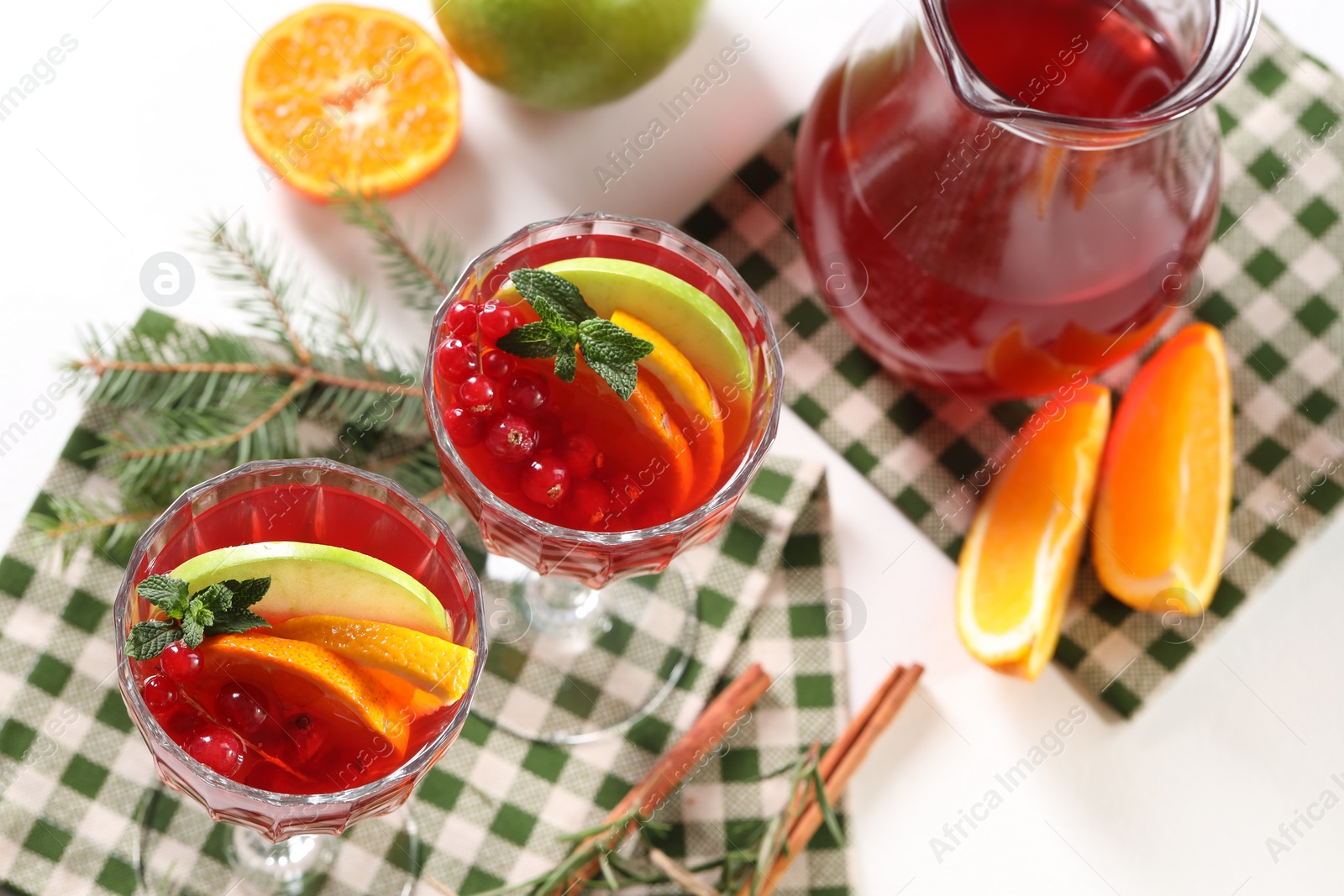 Photo of Christmas Sangria cocktail in glasses and jug, ingredients and fir tree branch on white table, above view