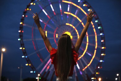 Photo of Beautiful young woman against glowing Ferris wheel in amusement park, back view