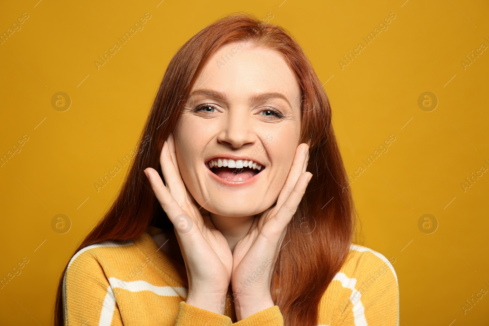 Photo of Candid portrait of happy young woman with charming smile and gorgeous red hair on yellow background