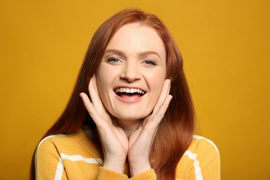Candid portrait of happy young woman with charming smile and gorgeous red hair on yellow background
