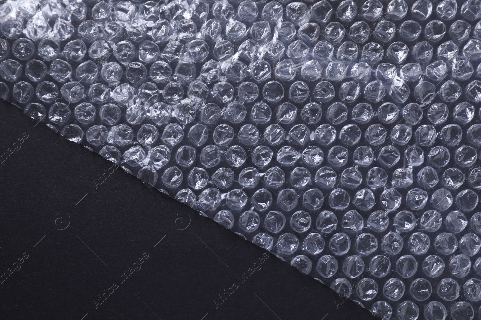 Photo of Transparent bubble wrap on black background, top view. Space for text