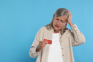 Upset woman with credit card became fraud victim on light blue background. Space for text