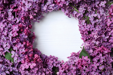 Photo of Frame made with beautiful lilac blossom on white wooden background, top view. Space for text