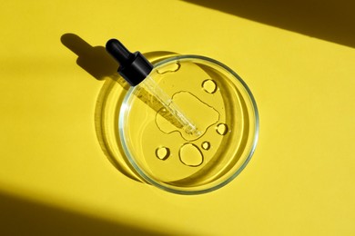 Photo of Petri dish with pipette on yellow background, top view