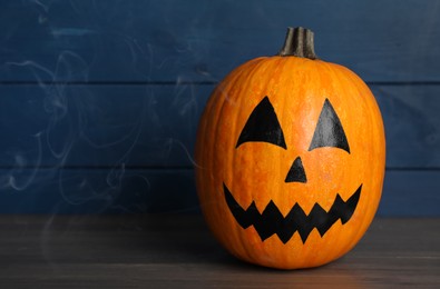 Photo of Pumpkin with drawn spooky face on wooden table, space for text. Halloween celebration
