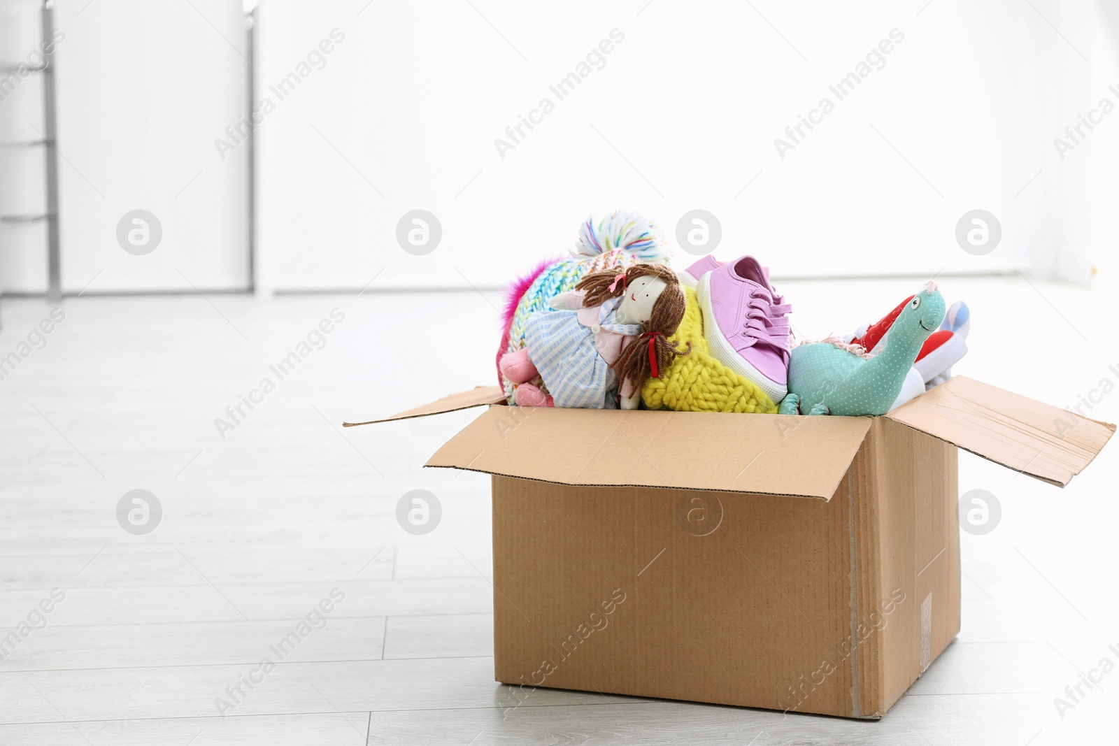 Photo of Donation box with clothes and toys on floor indoors. Space for text