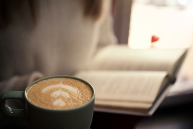 Photo of Woman with coffee reading book indoors, focus on cup