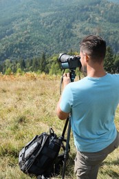 Photo of Professional photographer taking picture with modern camera in mountains, back view