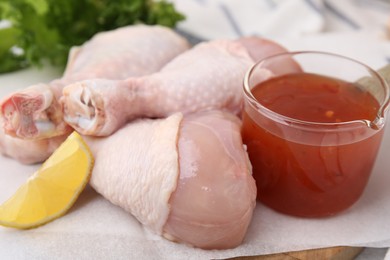 Photo of Fresh marinade, raw chicken drumsticks and lemon wedge on table, closeup