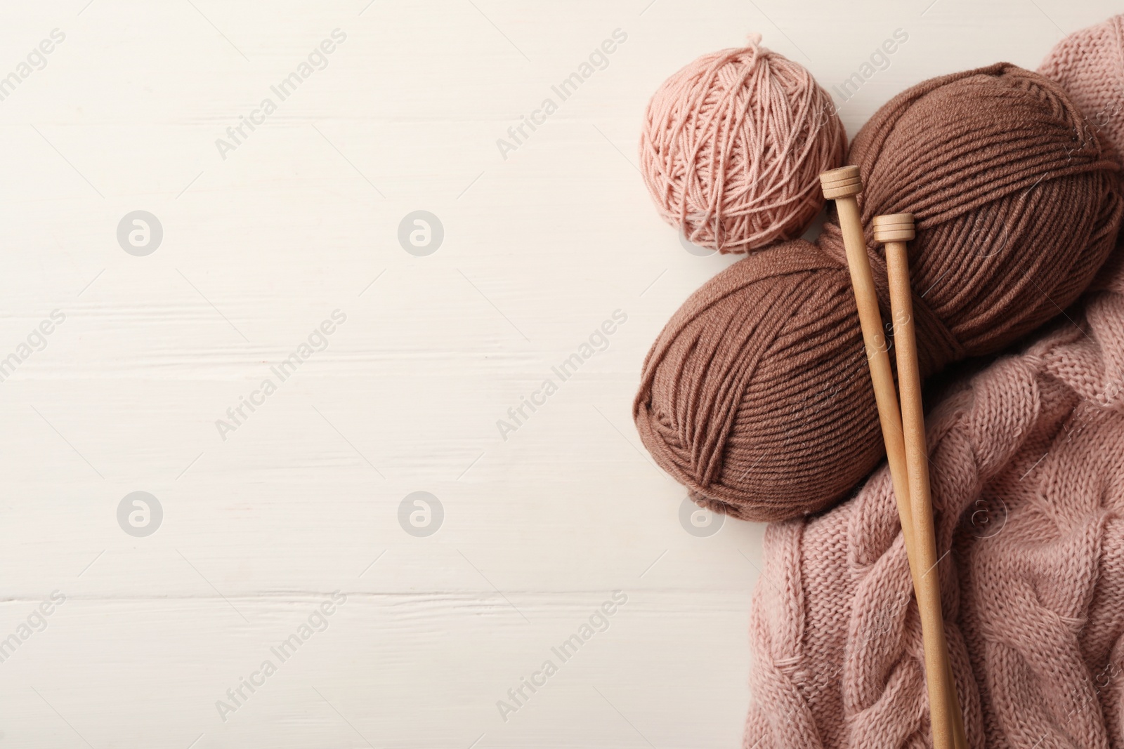 Photo of Woolen yarns, knitting needles and sweater on white wooden background, flat lay. Space for text