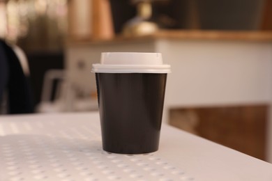 Photo of Takeaway paper cup with plastic lid on white table indoors