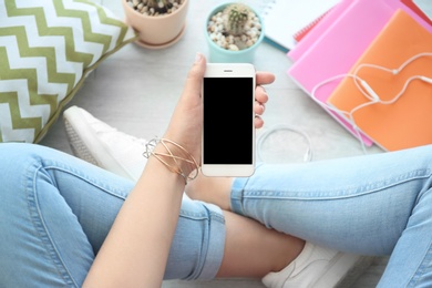 Photo of Young woman holding mobile phone with blank screen in hand, indoors