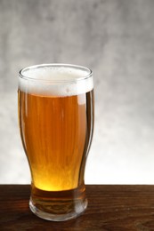 Photo of Glass with fresh beer on wooden table against light background