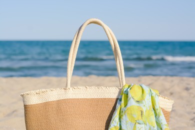 Photo of Straw bag with beach wrap on sandy seashore, closeup. Summer accessories
