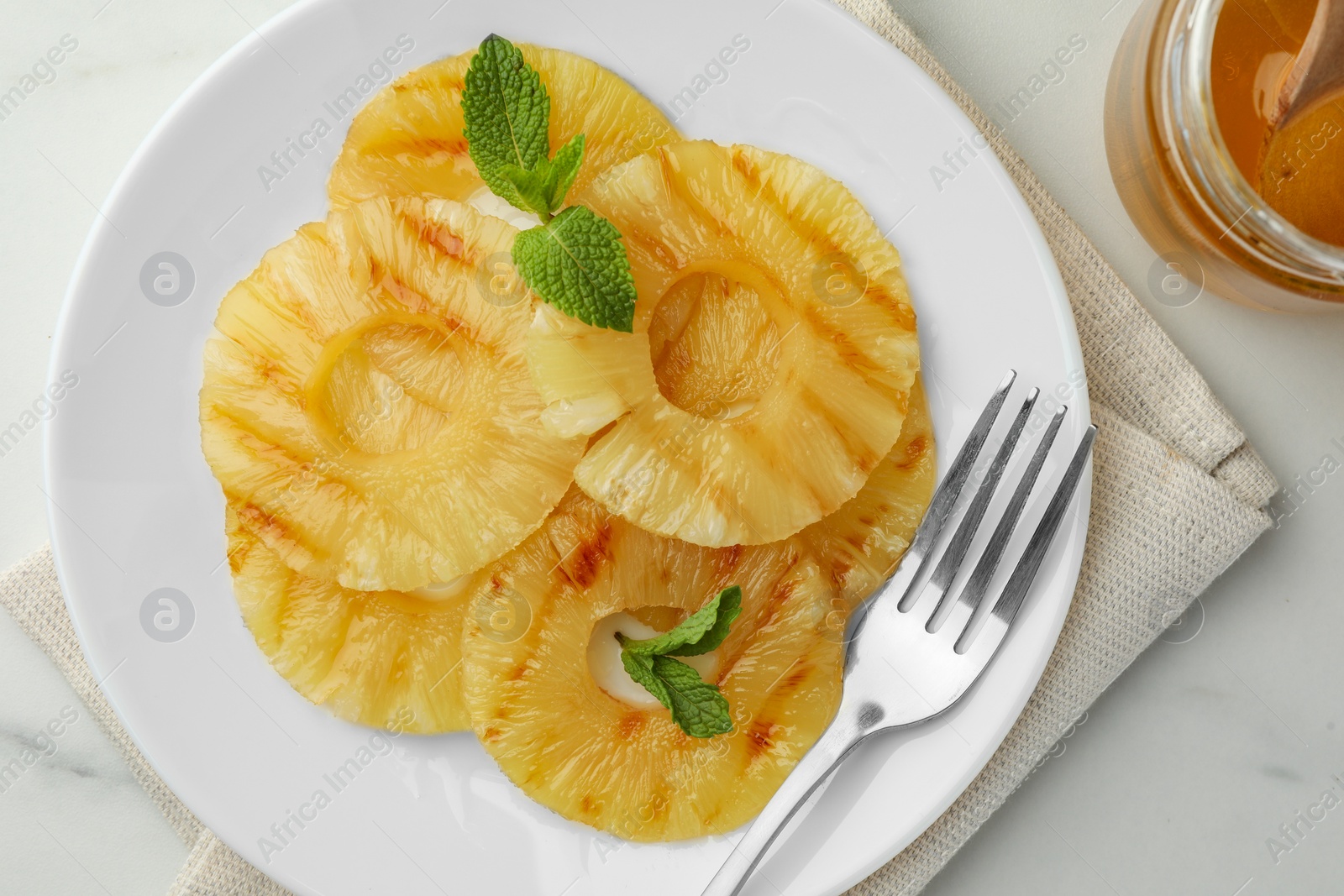 Photo of Tasty grilled pineapple slices, mint and honey on white table, flat lay