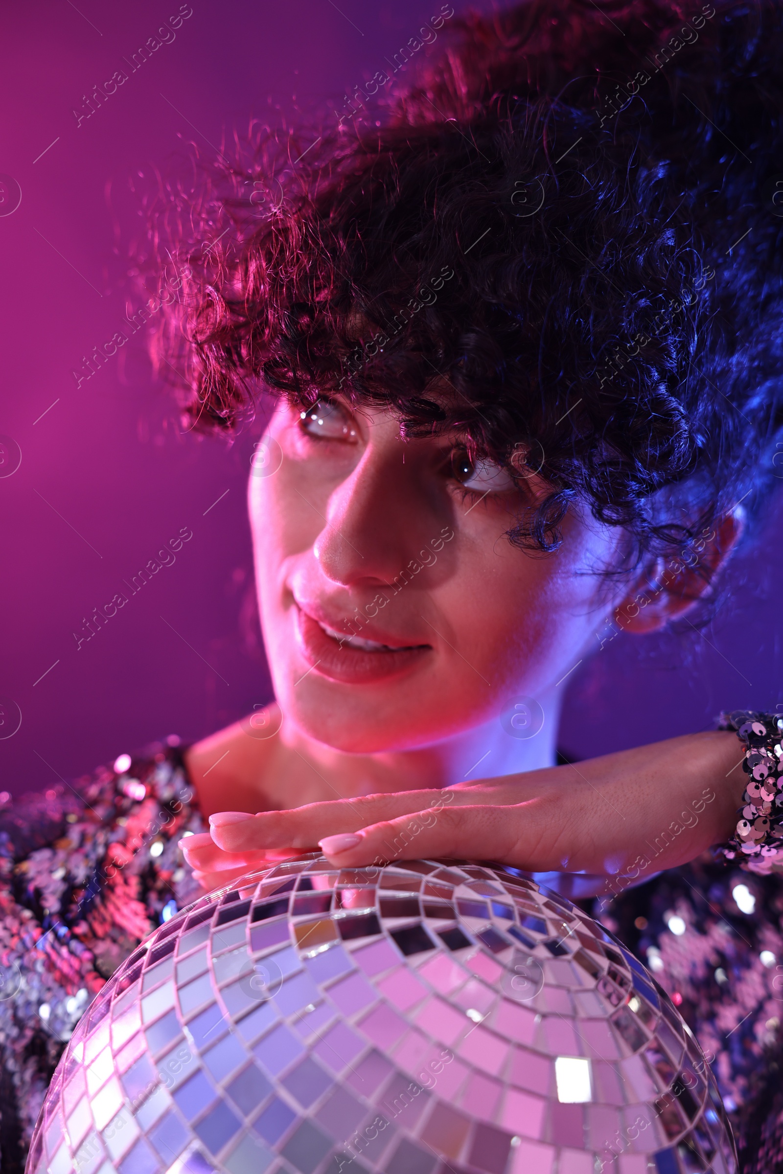 Photo of Beautiful young woman with disco ball posing on color background in neon lights, closeup