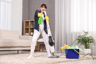 Photo of Happy young housewife with spray bottle having fun while cleaning carpet at home