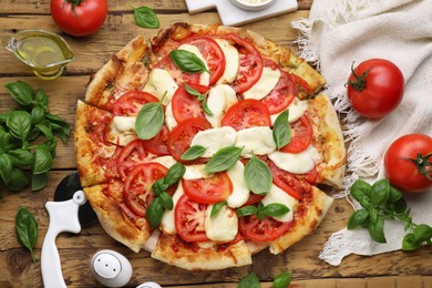 Photo of Delicious Caprese pizza with tomatoes, mozzarella and basil on wooden table, flat lay