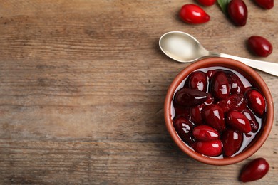 Photo of Delicious dogwood jam with berries and spoon on wooden table, flat lay. Space for text