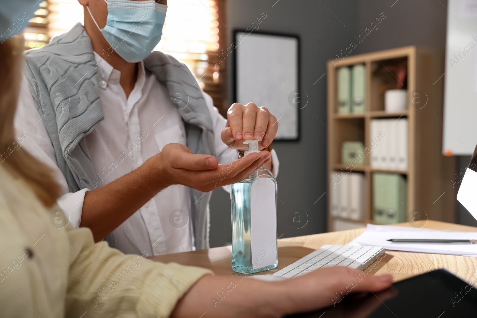 Photo of Office worker using hand sanitizer at table, closeup. Personal hygiene during COVID-19 pandemic